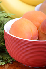 Image showing bananas and apricots on red plate, close up