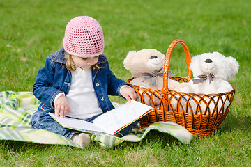 Image showing Happy three year old girl reading a book on a picnic