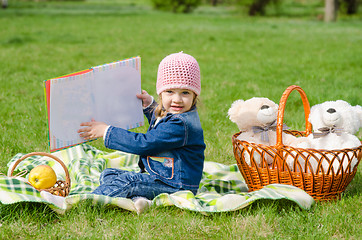 Image showing The three-year girl showing a book on a picnic
