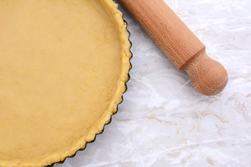 Image showing Baking tin lined with pastry, wooden rolling pin beside