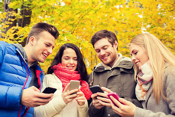 Image showing smiling friends with smartphones in city park