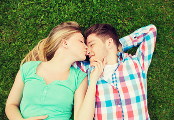 Image showing smiling couple lying on grass and kissing in park