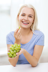 Image showing happy woman eating grapes at home