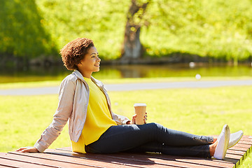 Image showing happy african woman drinks coffee at summer park 