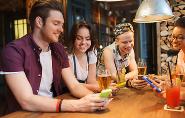 Image showing happy friends with smartphones and drinks at bar
