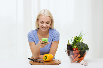 Image showing smiling woman with smartphone cooking vegetables