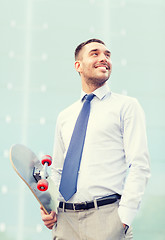 Image showing young smiling businessman with skateboard outdoors