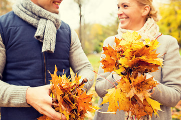 Image showing smiling couple with maple leaves in autumn park