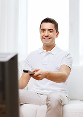 Image showing smiling man with remote control watching tv