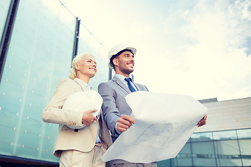 Image showing smiling businessmen with blueprint and helmets