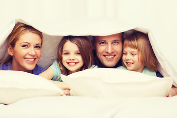 Image showing happy family with two kids under blanket at home