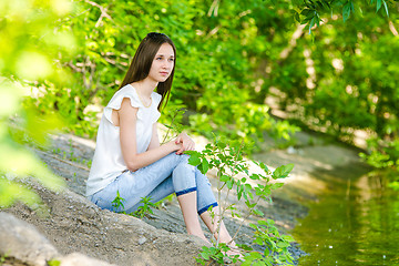 Image showing A girl sits on the concrete bank of the river