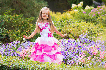 Image showing Happy little girl in a pink dress at flower bed