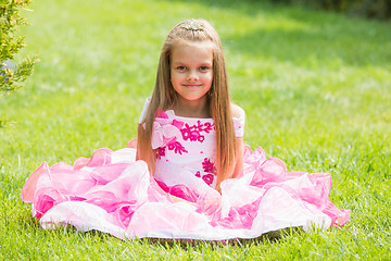 Image showing Five-year girl in a beautiful dress sat on the lawn in the green garden