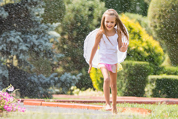 Image showing Girl with angel wings running around in the rain in the garden