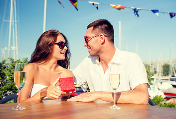 Image showing smiling couple with champagne and gift at cafe