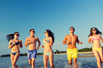 Image showing smiling friends in sunglasses running on beach