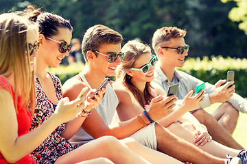 Image showing smiling friends with smartphones sitting on grass