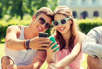 Image showing smiling friends with smartphones sitting in park