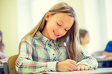 Image showing smiling school girl writing test in classroom