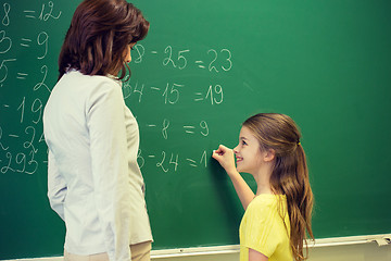 Image showing little smiling schoolgirl writing on chalk board