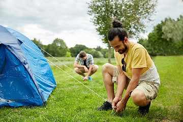 Image showing smiling friends setting up tent outdoors