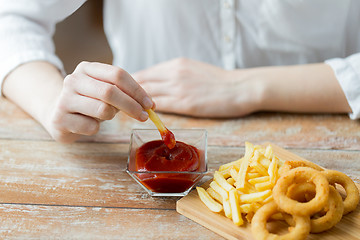 Image showing close up of hand dipping french fries into ketchup