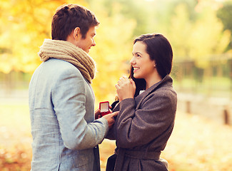 Image showing smiling couple with red gift box in autumn park