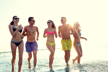 Image showing smiling friends in sunglasses running on beach