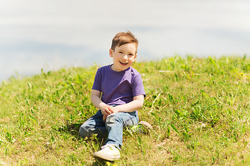 Image showing happy little boy sitting on grass outdoors