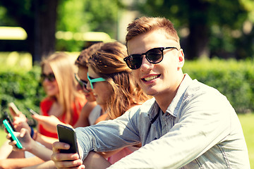 Image showing smiling friends with smartphones sitting in park