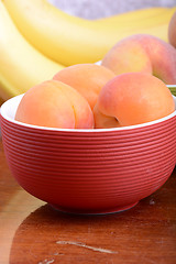 Image showing bananas and apricots on red plate, close up