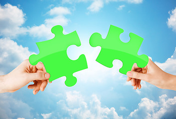 Image showing hands with green puzzle over sky background