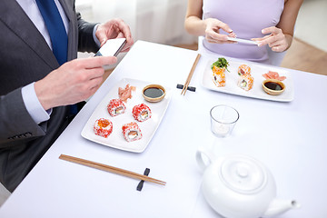 Image showing close up of couple with smartphones at restaurant