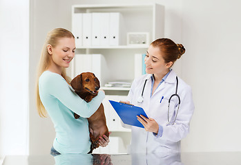 Image showing happy woman with dog and doctor at vet clinic