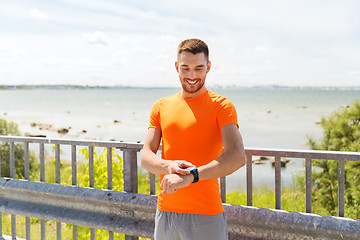 Image showing smiling young man with smart wristwatch at seaside