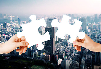 Image showing hands with green puzzle over city background