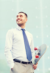 Image showing young smiling businessman with skateboard outdoors