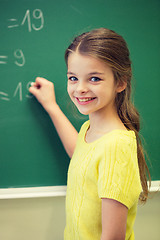 Image showing little smiling schoolgirl writing on chalk board