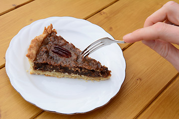 Image showing Woman uses dessert fork to cut into a slice of pecan pie