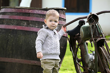 Image showing 2 years old curious Baby boy walking around the old bike 