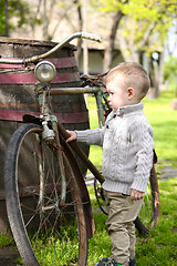 Image showing 2 years old curious Baby boy walking around the old bike 