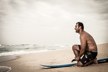 Image showing Surfer tying his surfboard\'s leach