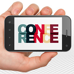 Image showing Finance concept: Hand Holding Smartphone with Conference on  display
