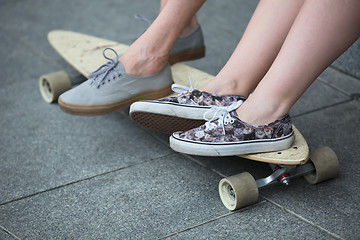 Image showing Feet couple of teenagers in sneakers on longboard closeup