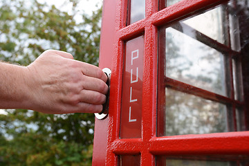 Image showing Man\'s hand pulls open red door of phone box