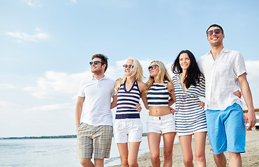 Image showing smiling friends in sunglasses walking on beach