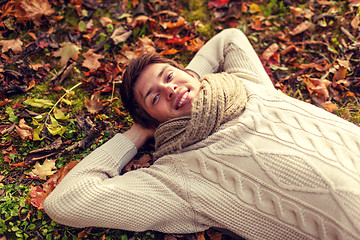 Image showing close up of smiling young man lying in autumn park