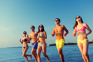 Image showing smiling friends in sunglasses running on beach