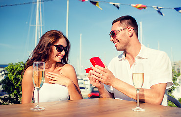 Image showing smiling couple with champagne and gift at cafe